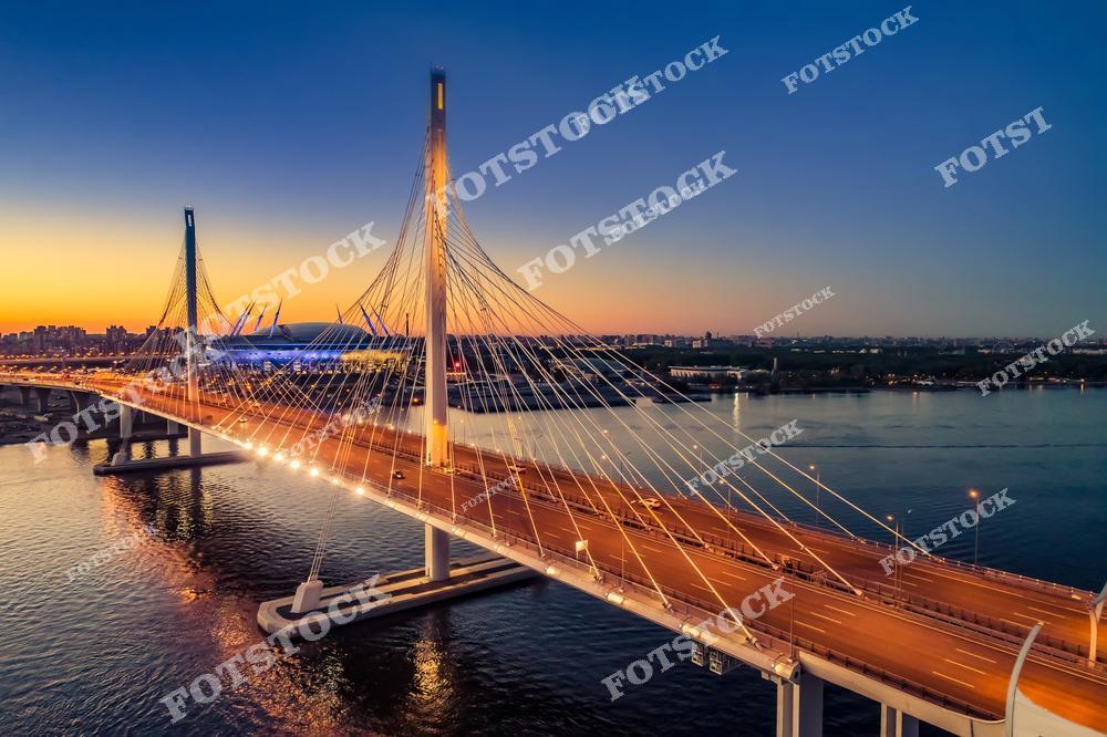 Панорамная фотография Санкт-Петербурга с высоты птичьего полета, на которой видны река Нева, мосты, улицы и районные дороги города. Съемка с дрона позволяет оценить масштабы городской инфраструктуры, архитектуру исторического и современного центра, а также красоту набережных и транспортной сети Северной столицы России. Фотография передает атмосферу города, гармонию городской среды с водными пространствами и панорамные виды мостов и улиц Петербурга. Снимок идеально подходит для туристических публикаций, фотостоков, рекламы, оформления интерьеров и материалов о городской инфраструктуре.